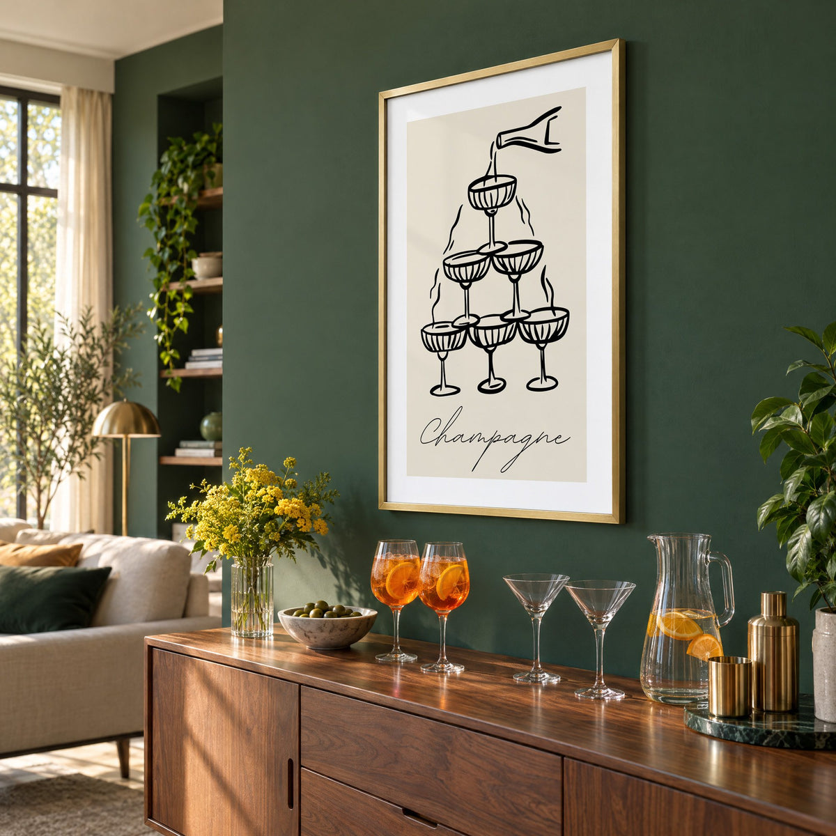 Champagne coupe tower black line-art print in a brass frame on a bottle green wall above a sideboard with spritz and martini glasses, seen at an angle