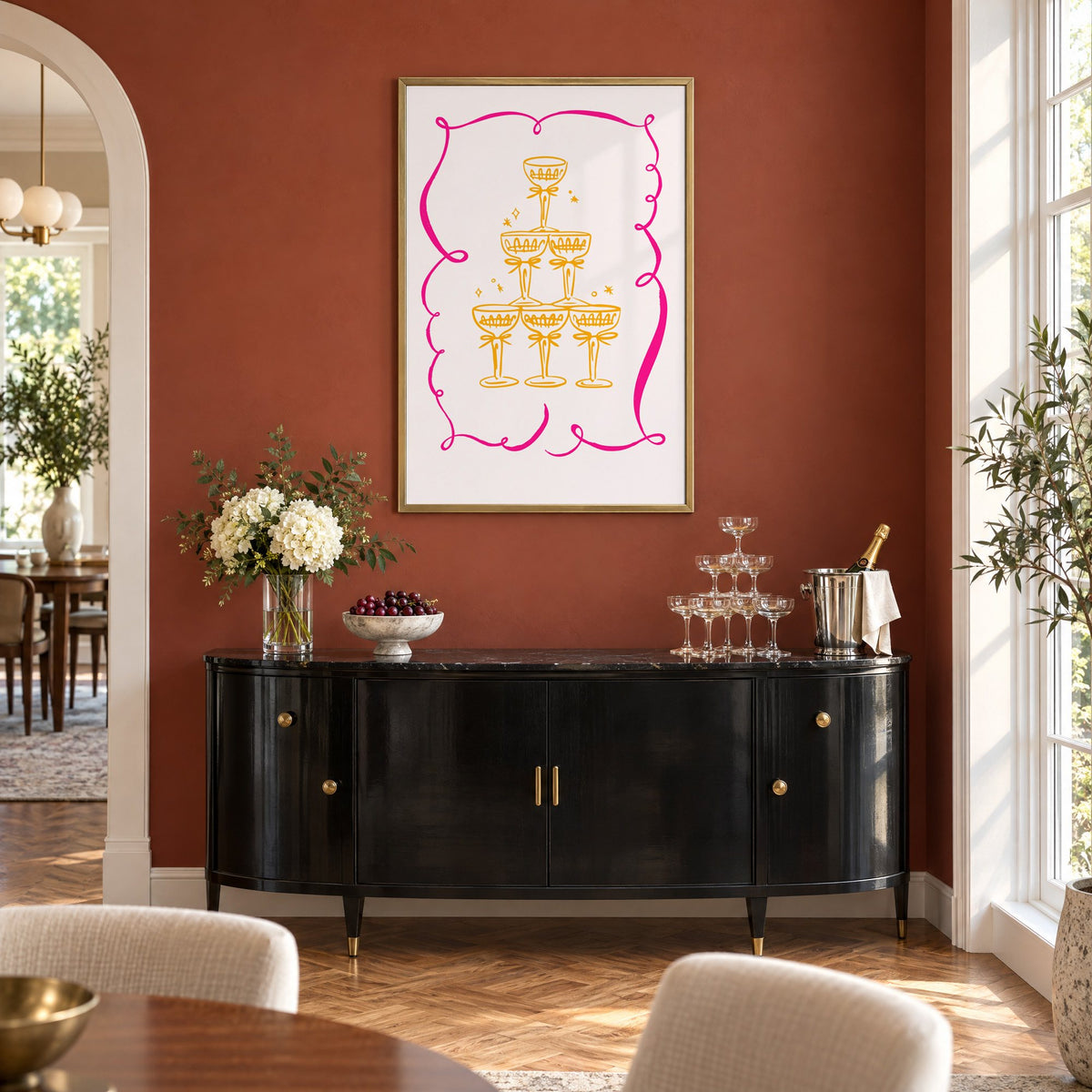 Champagne tower pink ribbon frame print in a brass frame on a terracotta wall above a black buffet with a champagne tower
