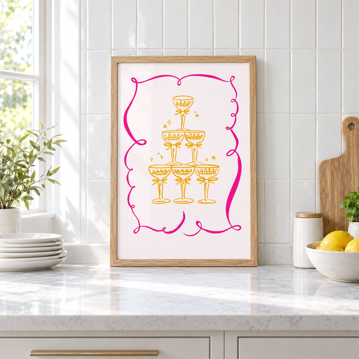 Champagne tower pink ribbon frame print in an oak frame leaning on a marble counter by white tiles and lemons