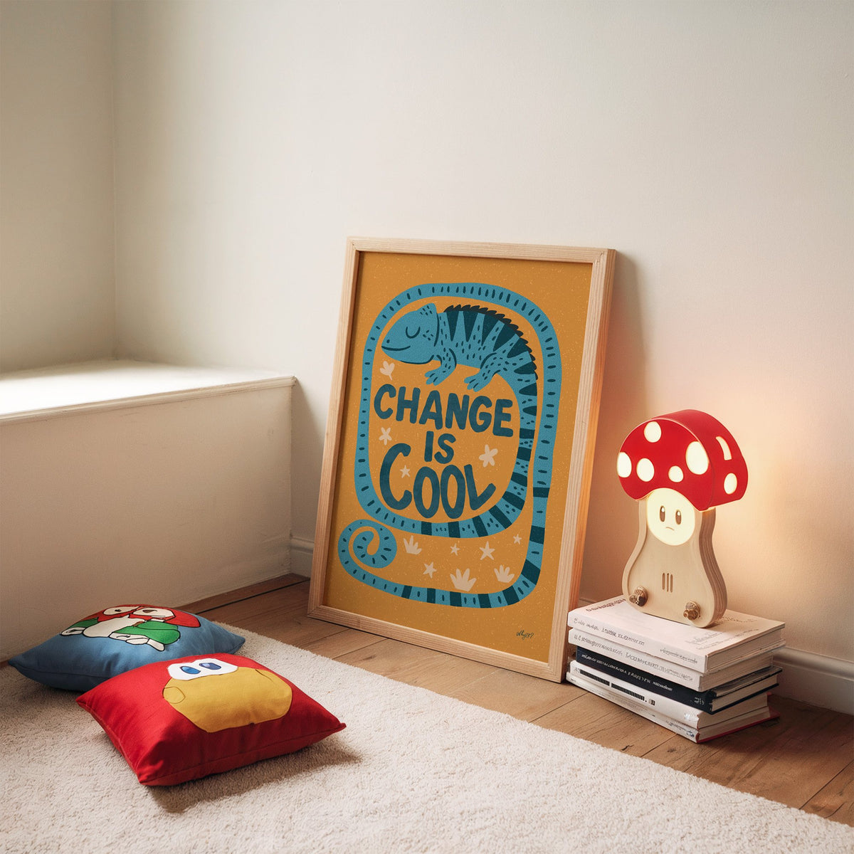Change is cool chameleon orange nursery print in an oak frame leaning on a rug beside a mushroom lamp and floor cushions