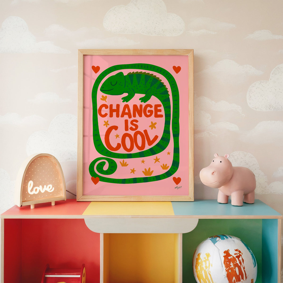 Change is cool chameleon pink nursery print in an oak frame on a rainbow toy shelf against cloud wallpaper