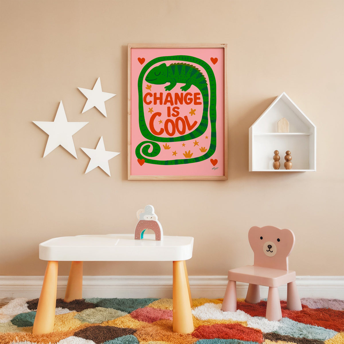 Change is cool chameleon pink nursery print in an oak frame on a peach wall above a kids table with wall stars