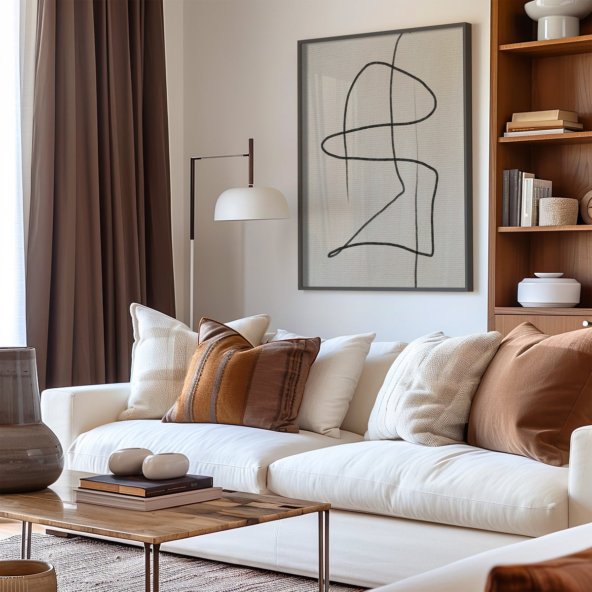 Charcoal continuous loop line art print in a black frame above a cream sofa with brown striped pillows