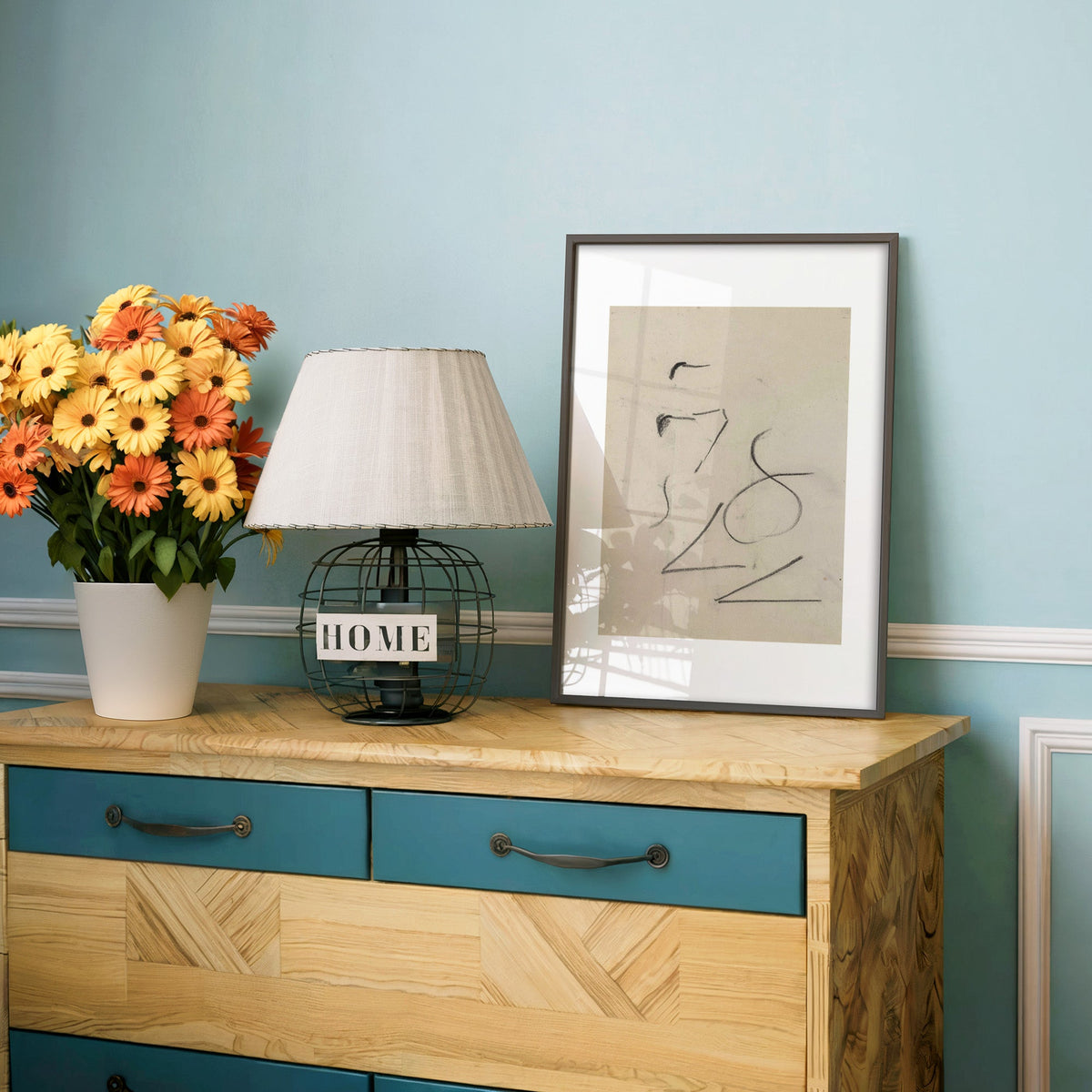 Charcoal figure eight strokes line art print in a charcoal frame on a teal dresser beside orange and yellow daisies
