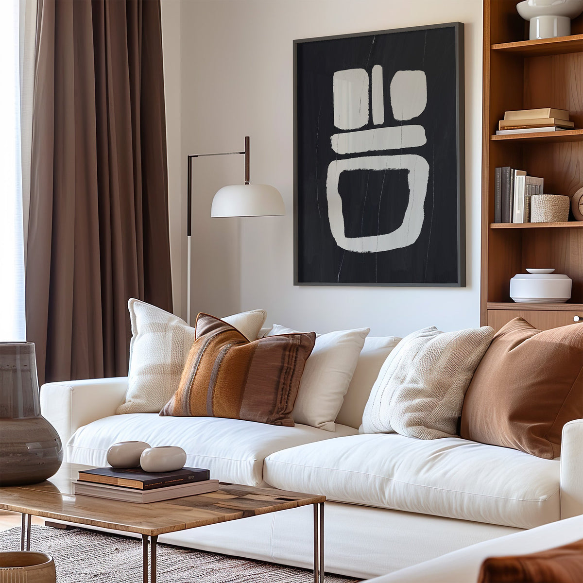 Charcoal totem blocks with white paint print in a black frame above a cream sofa with brown striped pillows