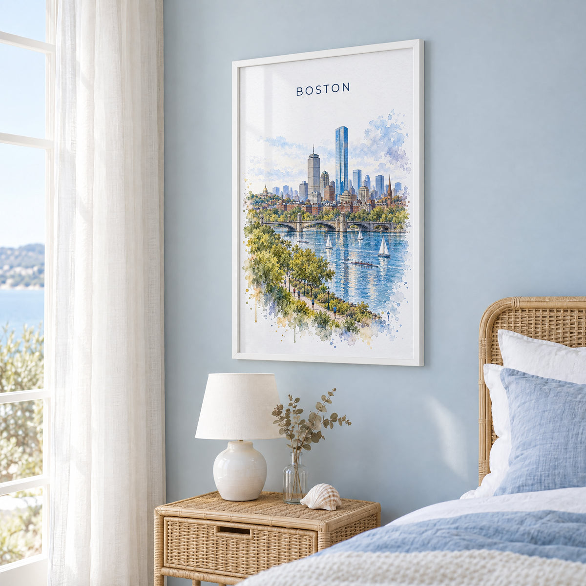 Charles River Boston watercolor print in a white frame on a pale blue wall beside a rattan bed in a coastal bedroom