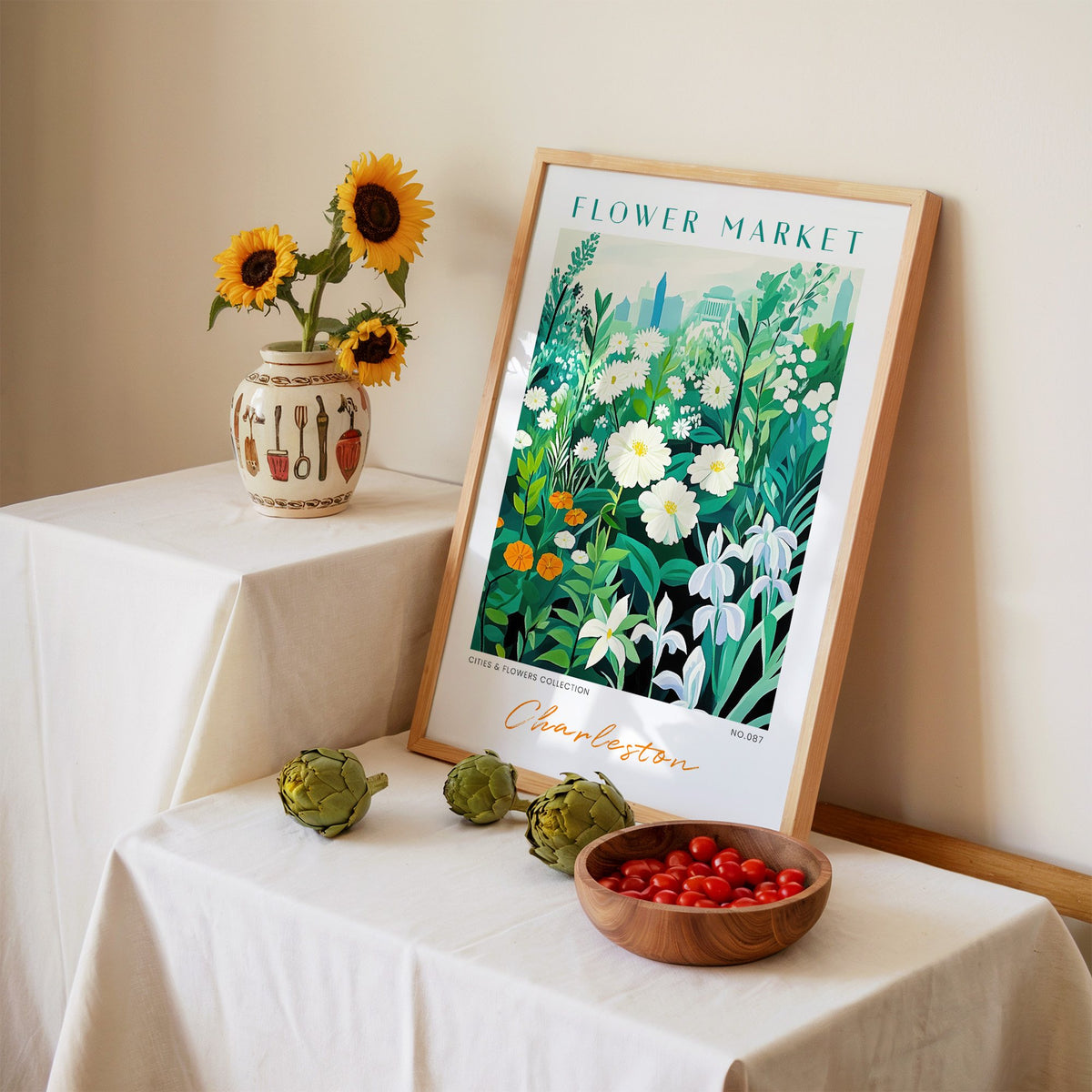 Charleston flower market print in an oak frame leaning on a linen-draped table beside a vase of sunflowers