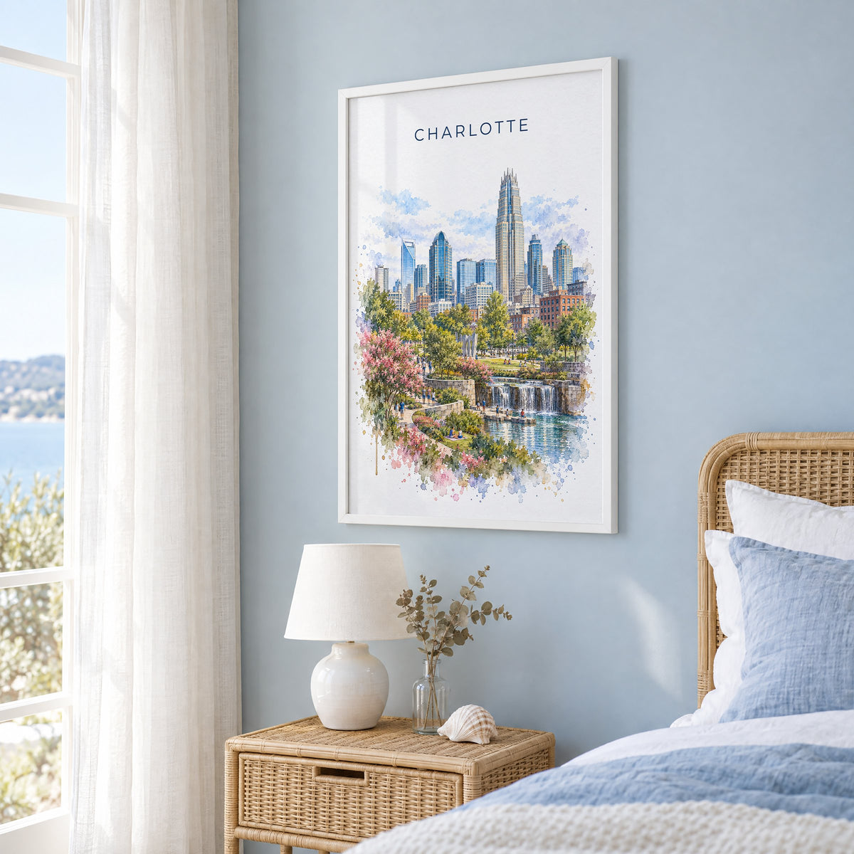 Charlotte watercolor print in a white frame on a pale blue wall beside a rattan bed in a coastal bedroom