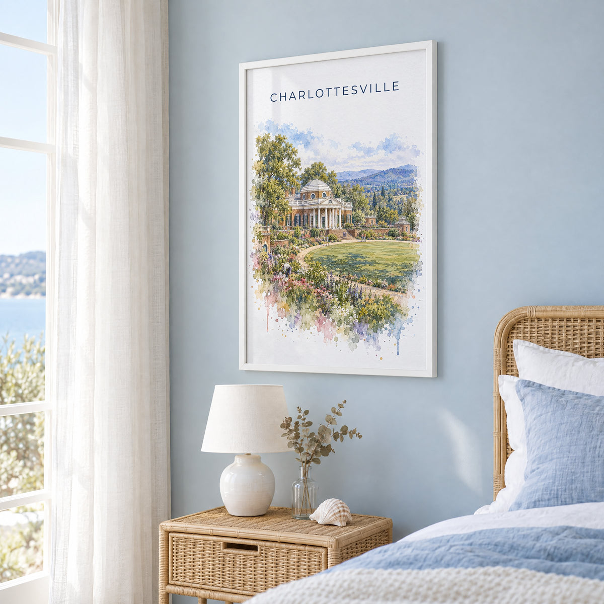 Charlottesville watercolor print in a white frame on a pale blue wall beside a rattan bed in a coastal bedroom