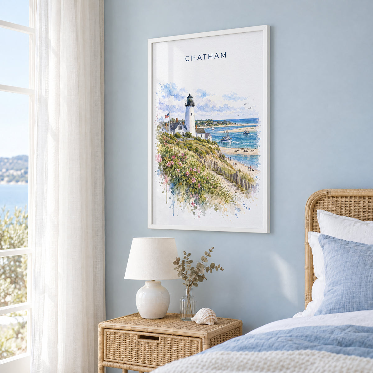 Chatham, Massachusetts watercolor print in a white frame on a pale blue wall beside a rattan bed in a coastal bedroom