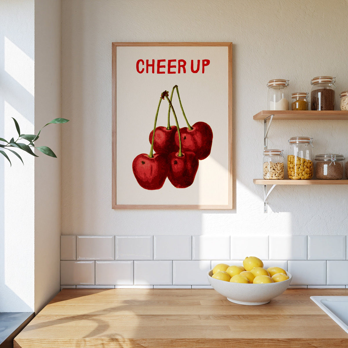 Cheer Up cherries print in an oak frame on a subway-tiled kitchen wall beside open shelves of pantry jars