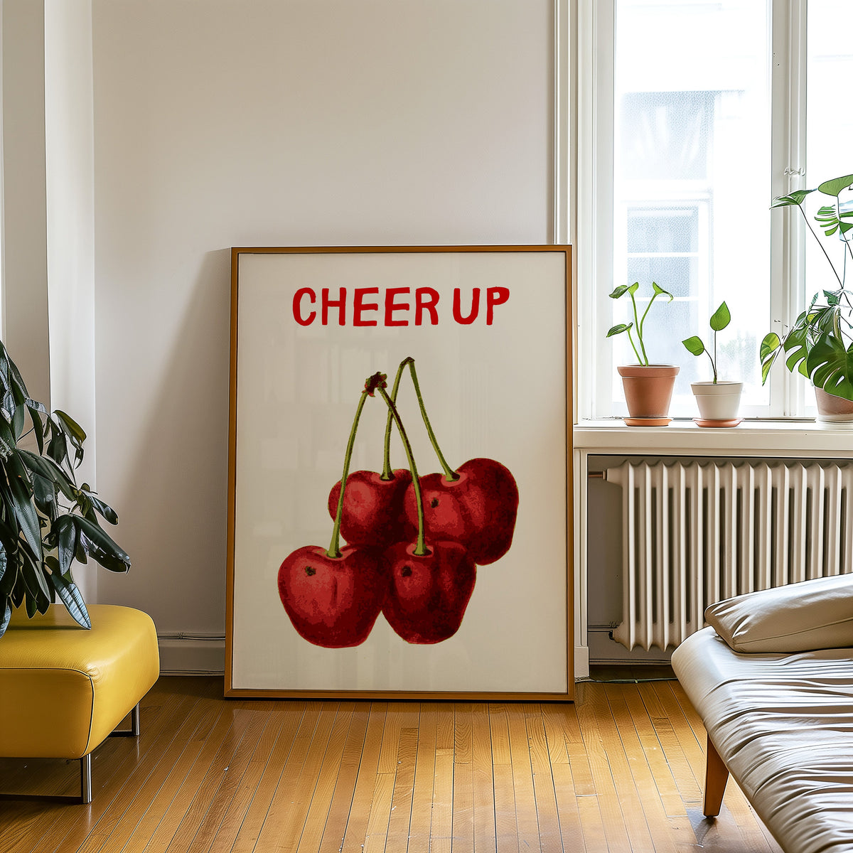 Cheer Up cherries print in an oak frame leaning on a wooden floor beside a yellow leather bench