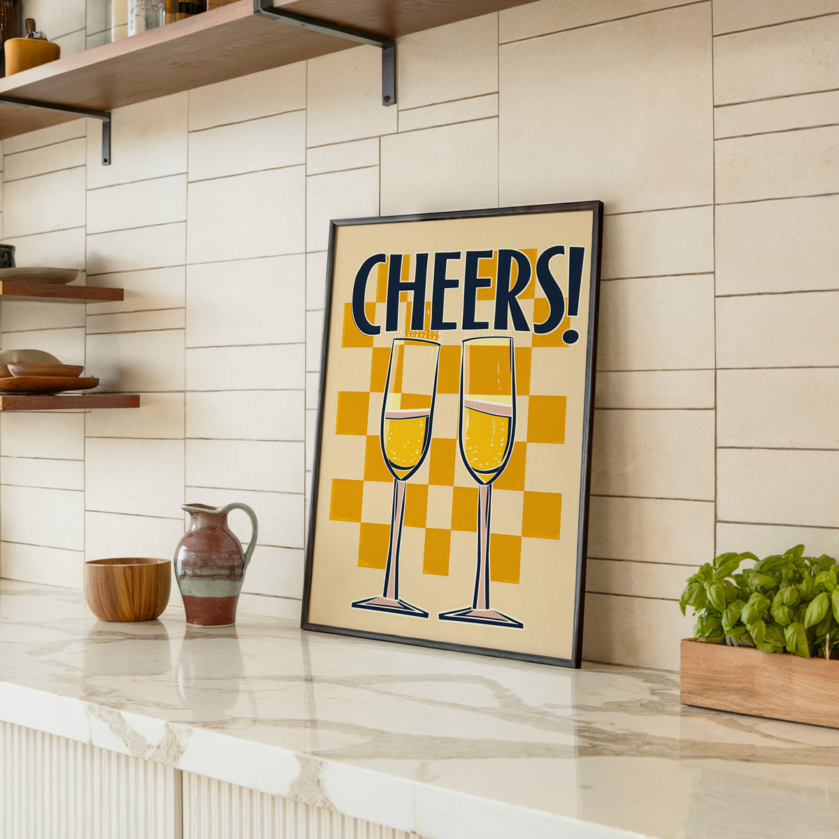 Cheers champagne flutes print in a black frame leaning on a marble counter in a tiled kitchen