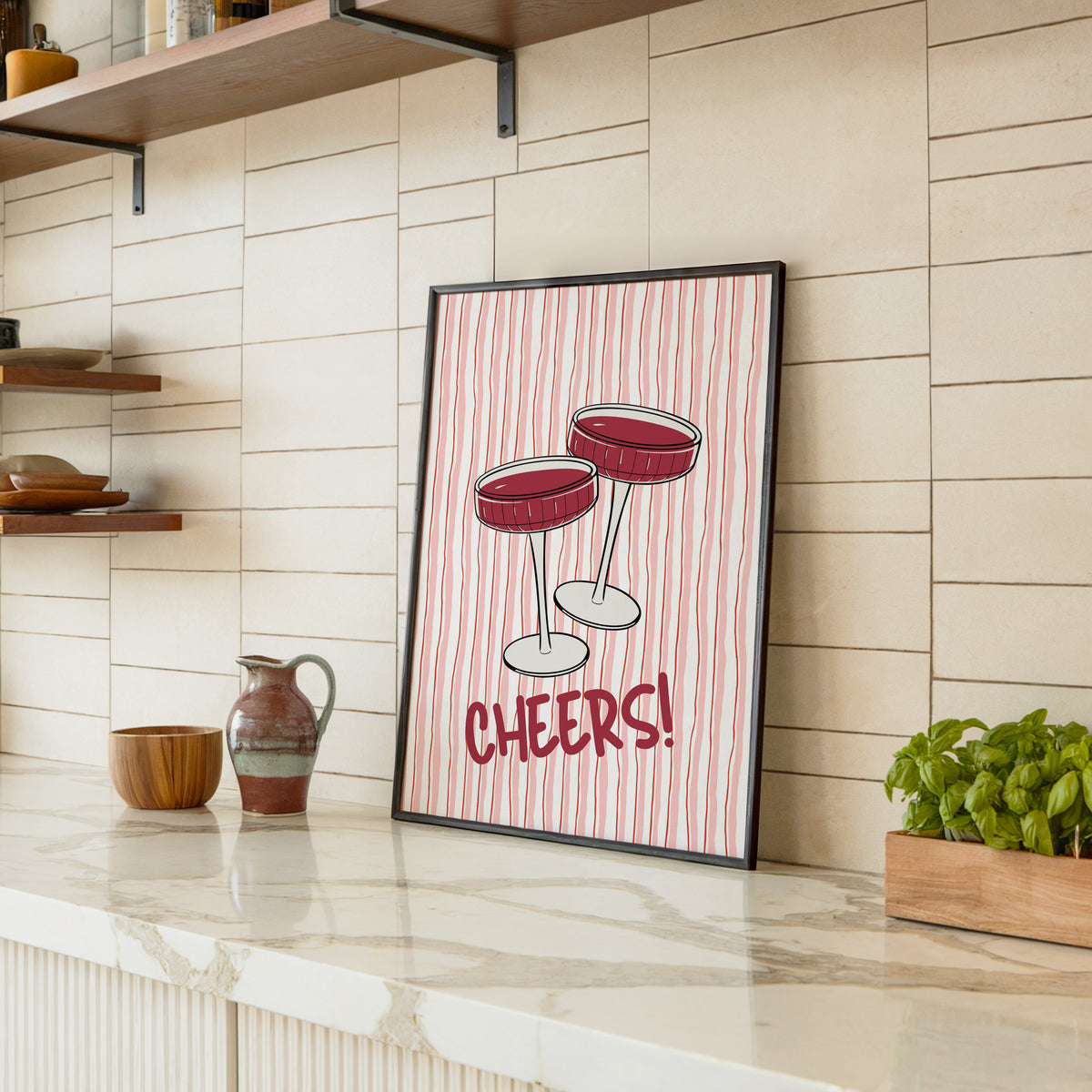 Cheers coupes print in a black frame leaning on a marble counter in a tiled kitchen