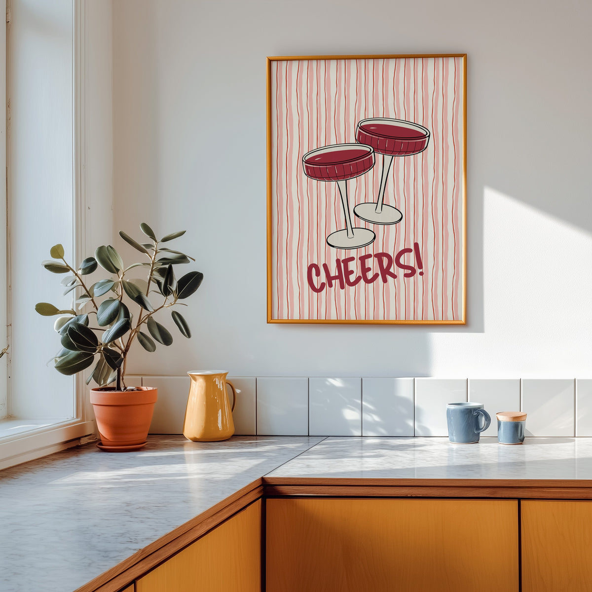 Cheers coupes print shown in a gold frame above a marble counter in a tan kitchen