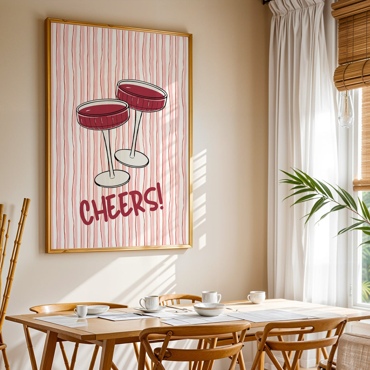 Cheers coupes print shown in a gold frame above a breakfast table by a curtained window