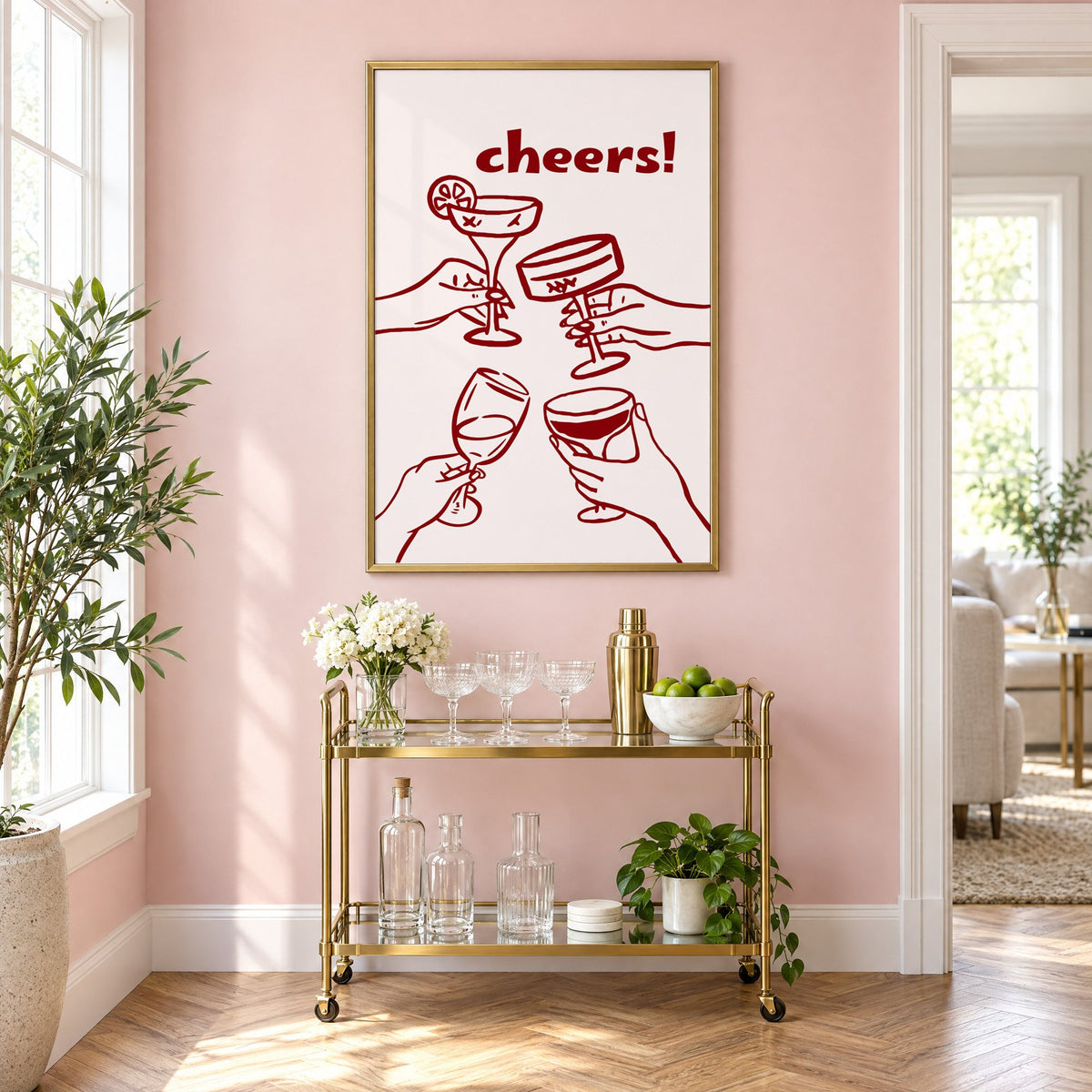 cheers! four hands toasting burgundy line print in a brass frame on a blush pink wall above a gold bar cart with glassware
