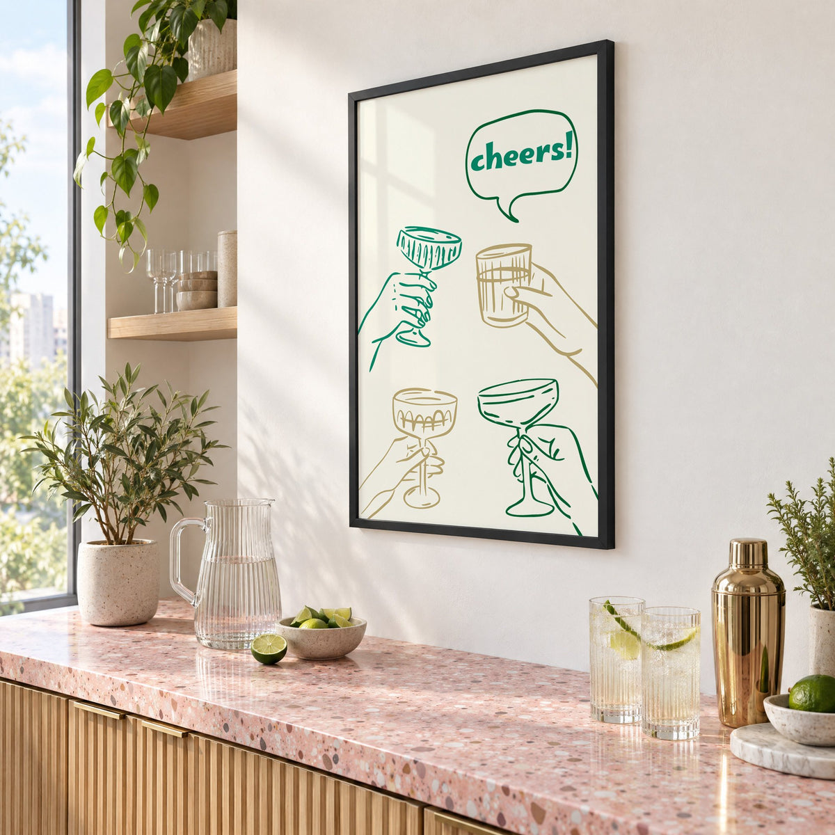 cheers! hands toasting coupes teal and gold print in a black frame above a pink terrazzo cocktail counter with limes, seen at an angle