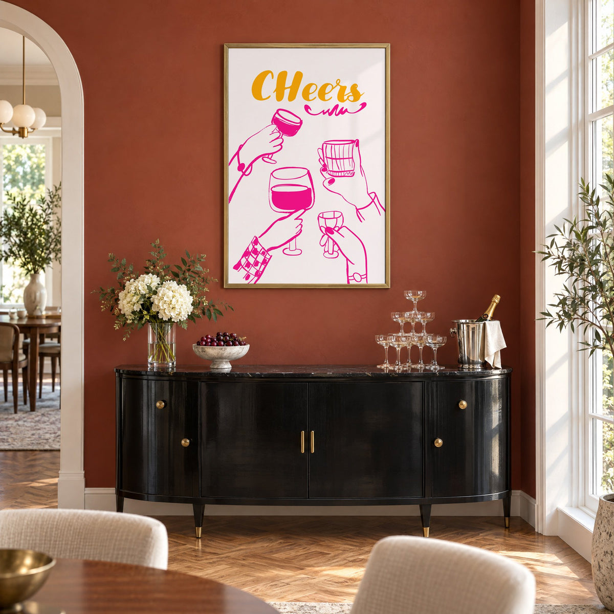 CHeers hot pink toasting hands print in a brass frame on a terracotta wall above a black buffet with a champagne tower