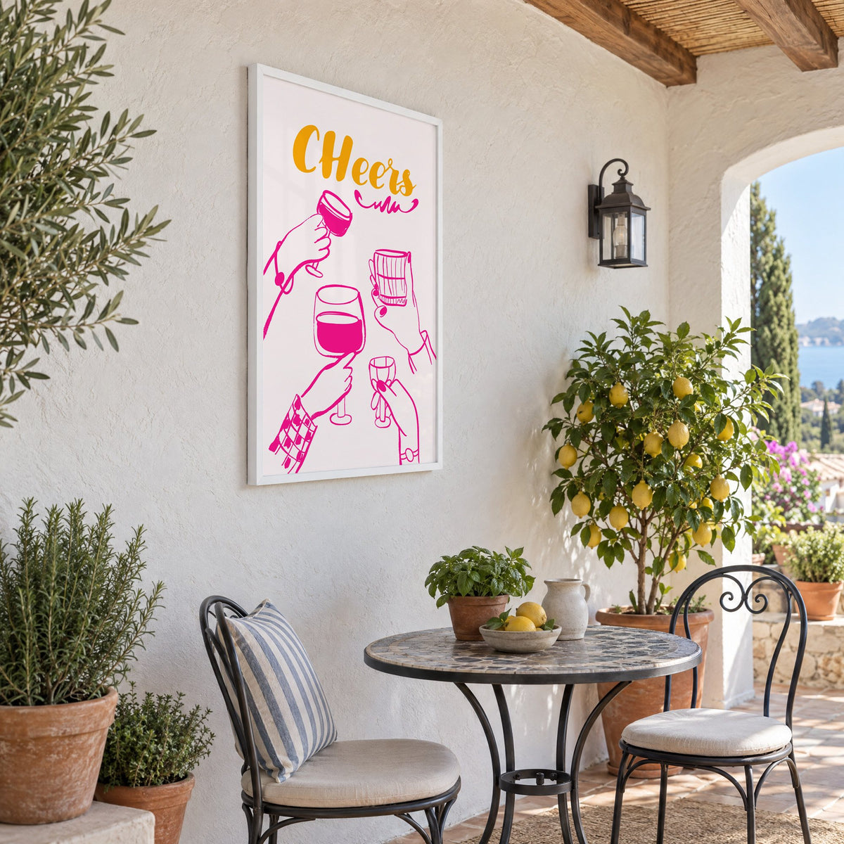 CHeers hot pink toasting hands print in a white frame on a sunny patio wall beside a potted lemon tree