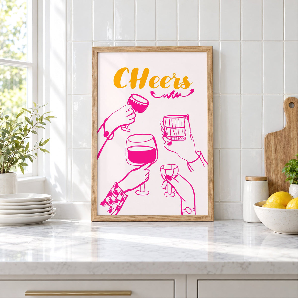 CHeers hot pink toasting hands print in an oak frame leaning on a marble counter by white tiles and lemons