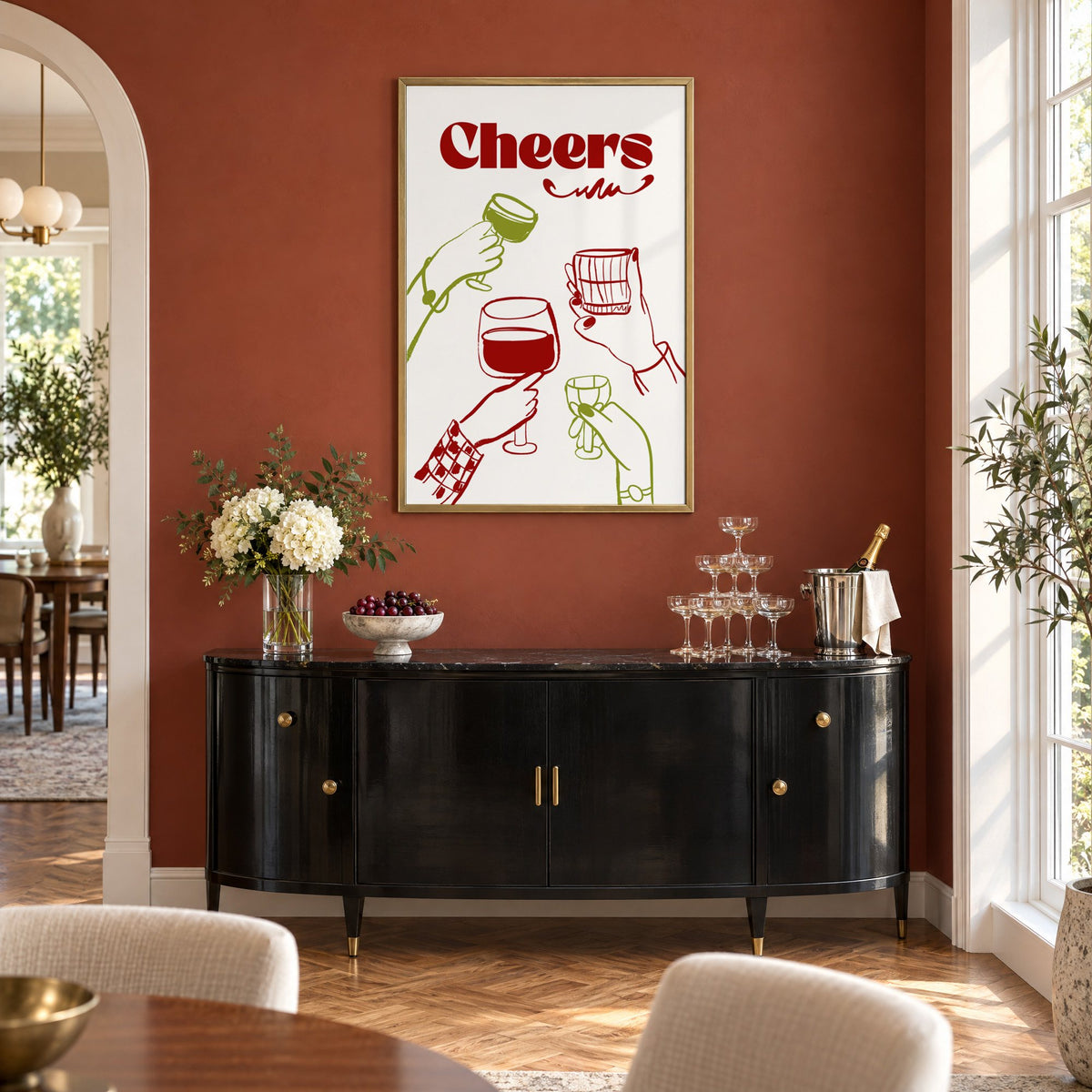 Cheers red and olive toasting hands print in a brass frame on a terracotta wall above a black buffet with a champagne tower