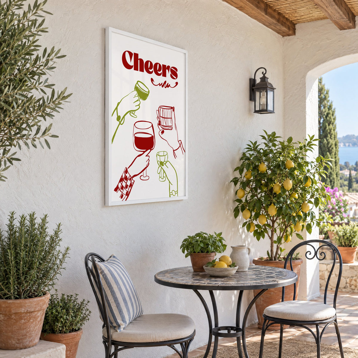 Cheers red and olive toasting hands print in a white frame on a sunny patio wall beside a potted lemon tree