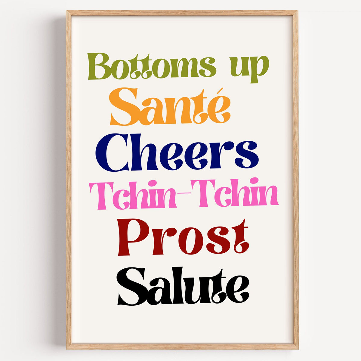 Cheers toasts colorful typography print in a light oak frame on a plain white wall