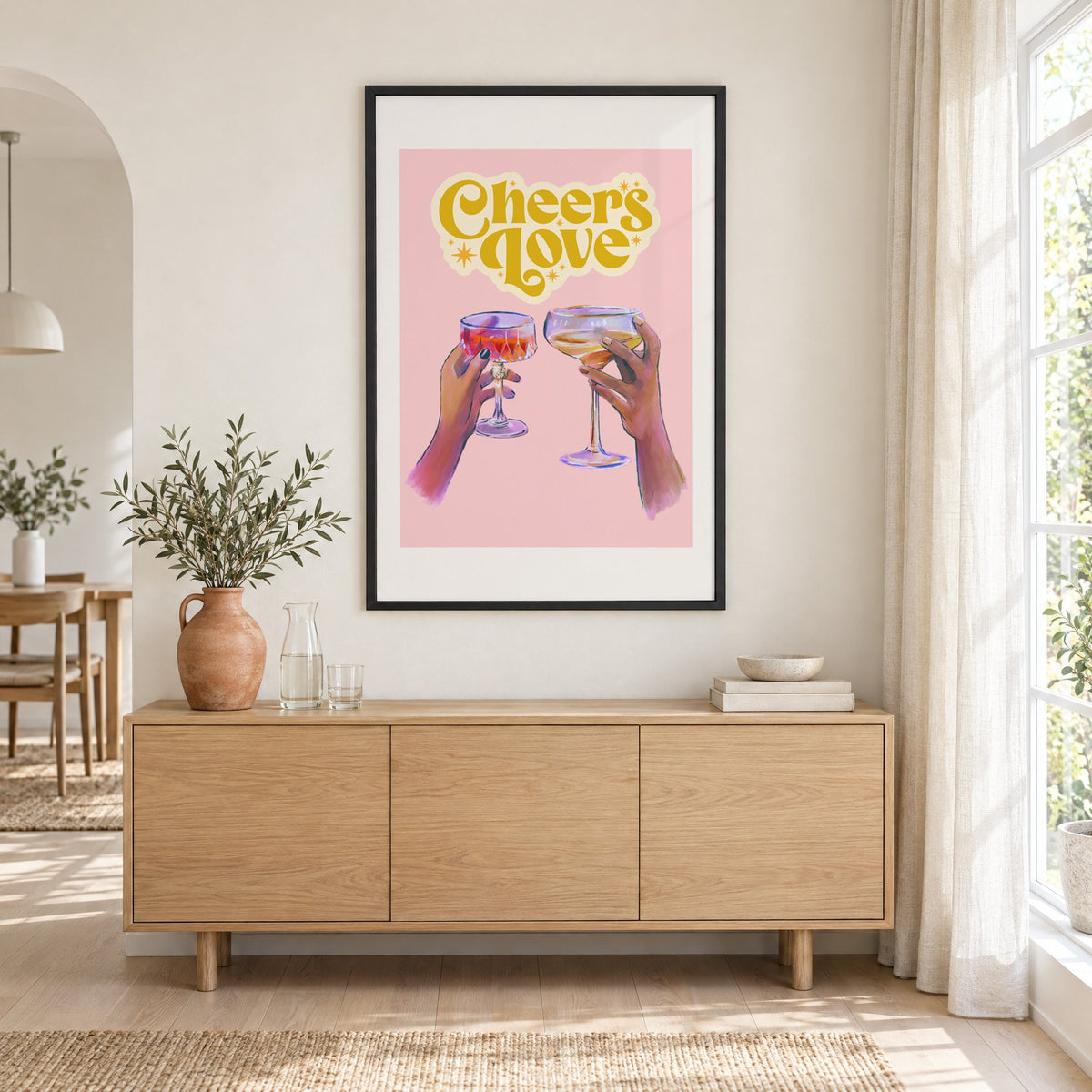 Cheers Love coupe toast print in a black frame above an oak sideboard with a terracotta vase of olive branches