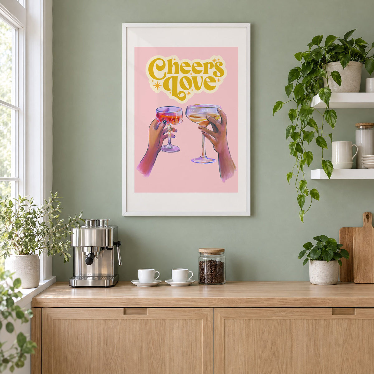 Cheers Love coupe toast print in a white frame on a sage green coffee nook wall above an espresso machine