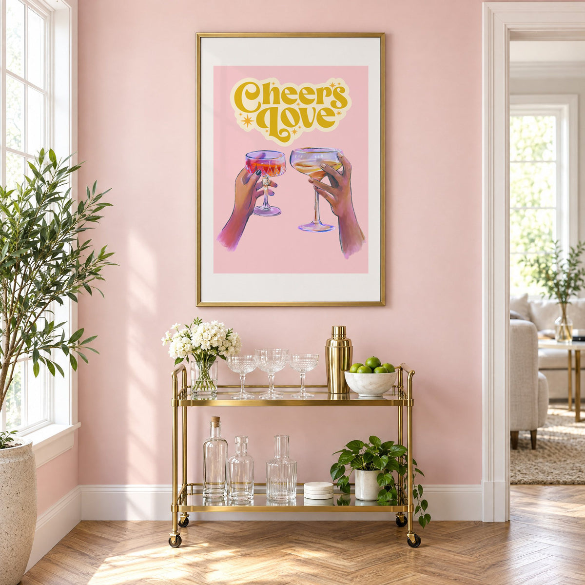 Cheers Love coupe toast print in a brass frame above a gold bar cart on a blush pink wall