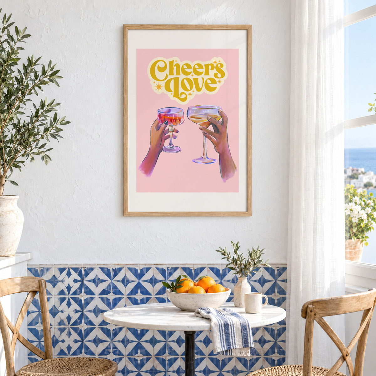 Cheers Love coupe toast print in an oak frame above a bistro table and blue patterned tiles