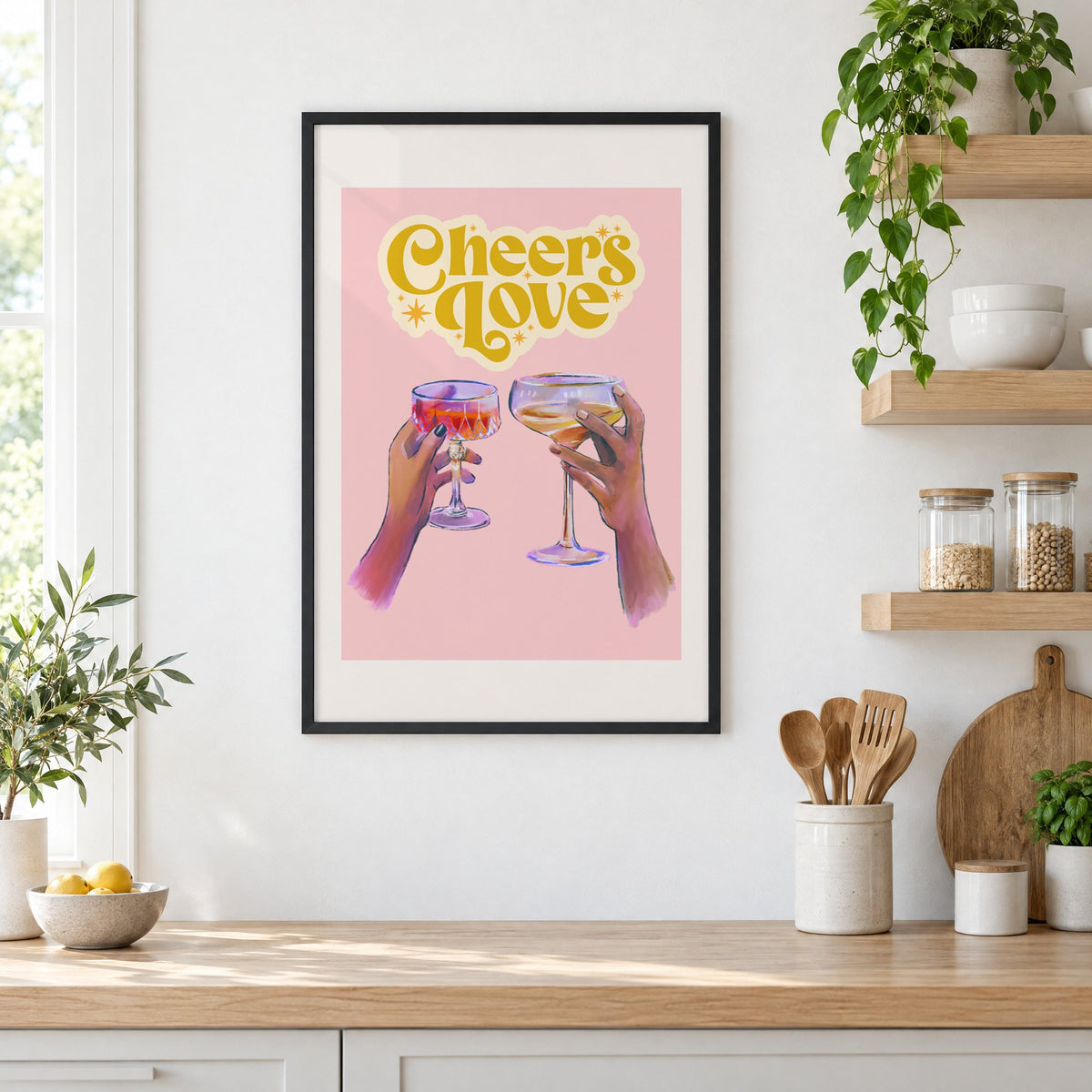 Cheers Love coupe toast print in a black frame in a white kitchen beside open wood shelves and glass jars