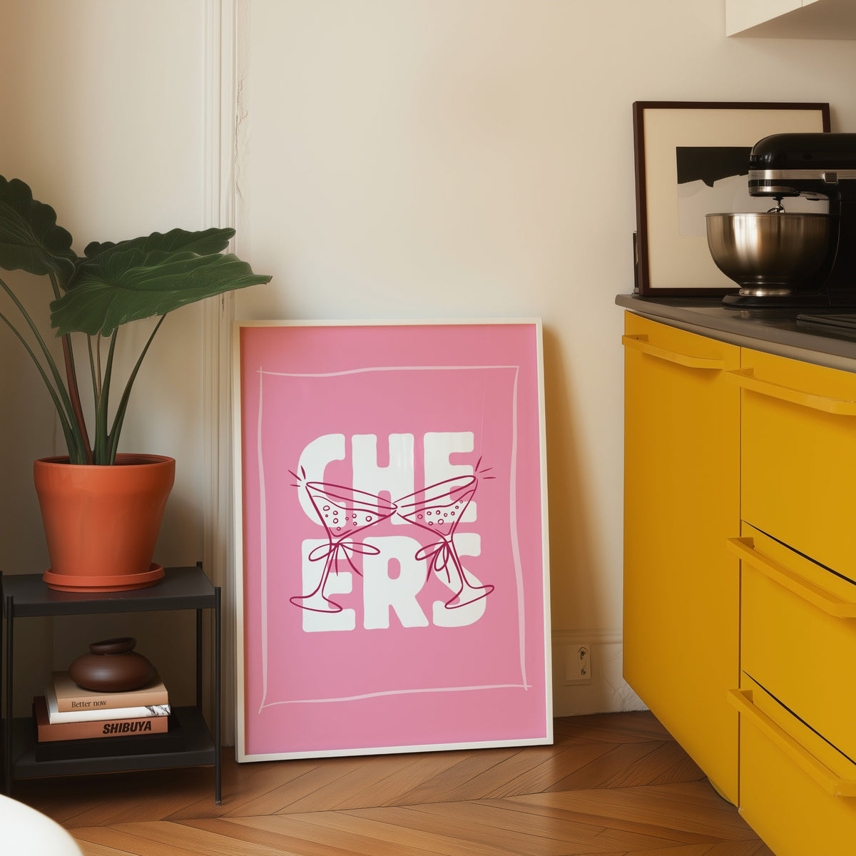 Cheers martini print in a white frame leaning on parquet beside a bright yellow kitchen