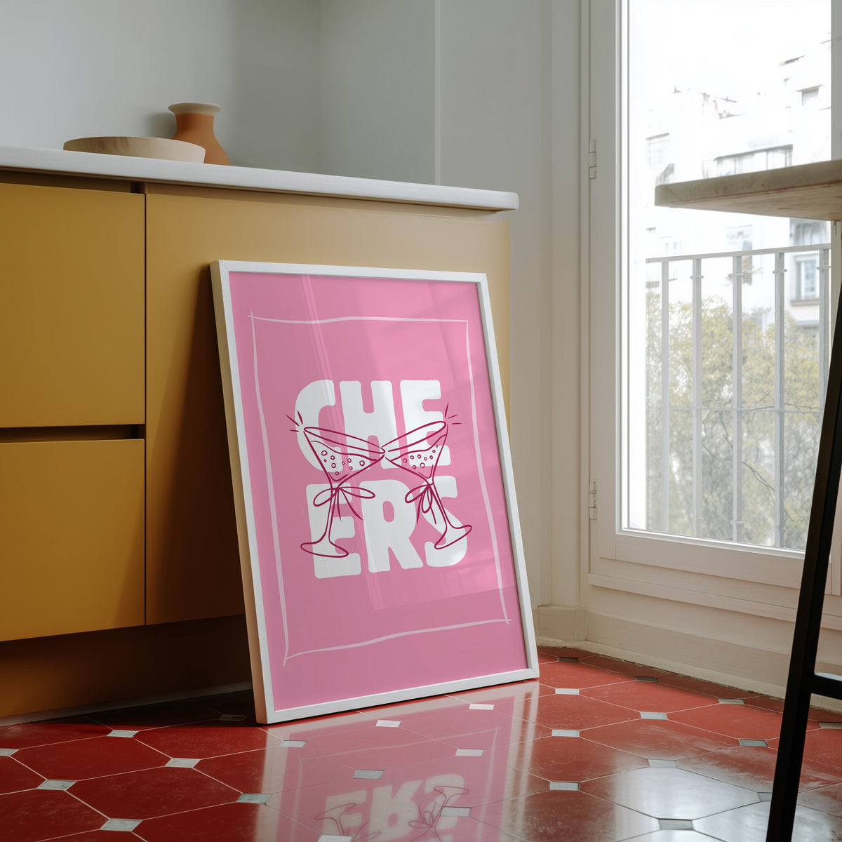 Cheers martini print in a white frame against yellow cabinets on a red tiled floor
