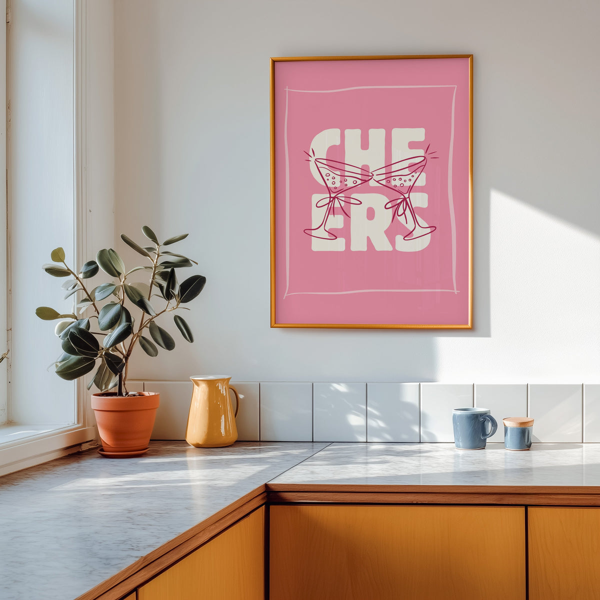 Cheers martini print in a gold frame above a marble counter with a yellow ceramic jug