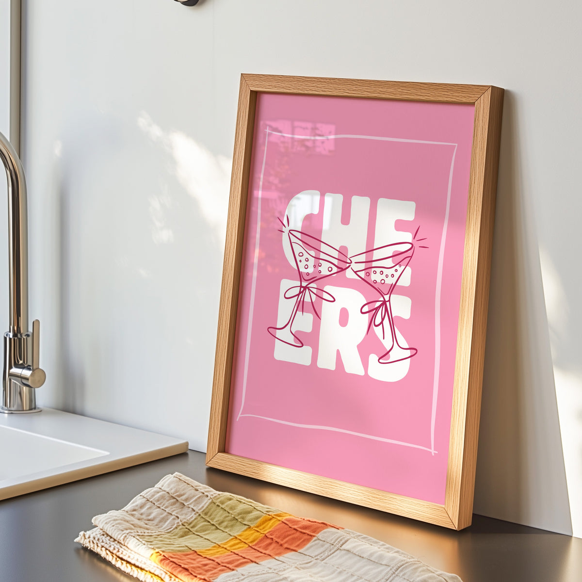 Cheers martini print in an oak frame by the kitchen sink beside a striped tea towel