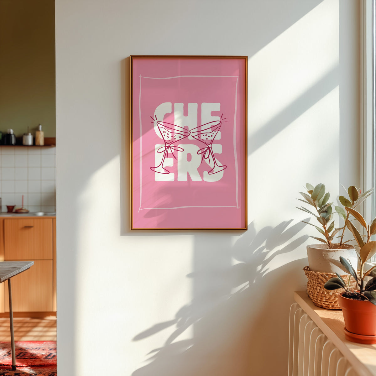 Cheers martini print in a gold frame in sunlight with plants on the ledge and a kitchen beyond