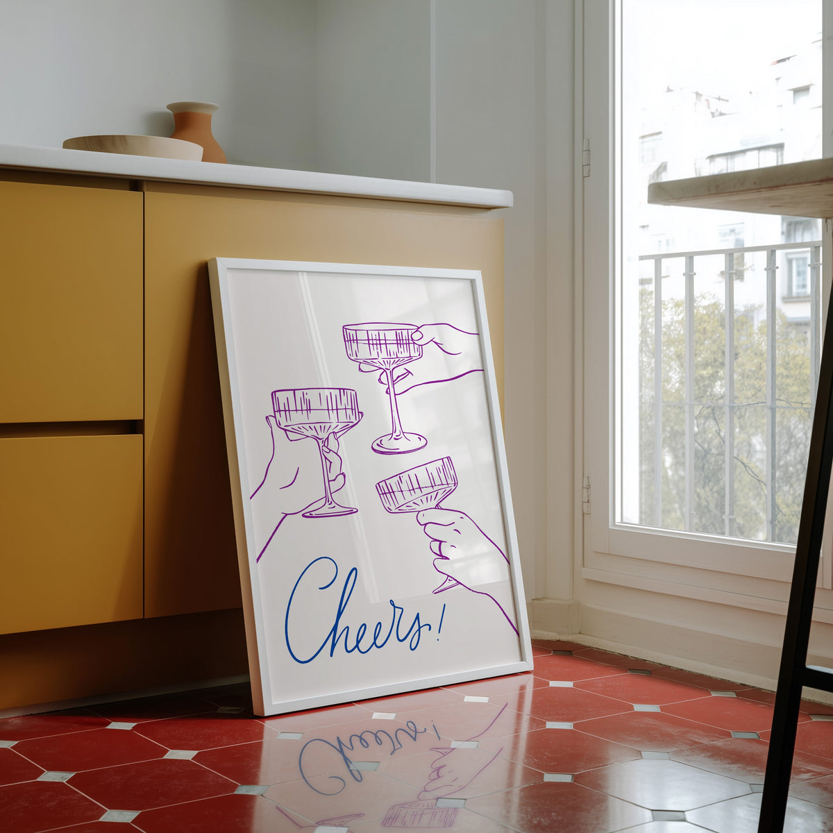 Cheers coupe glasses print in a white frame against yellow cabinets on a red tiled floor