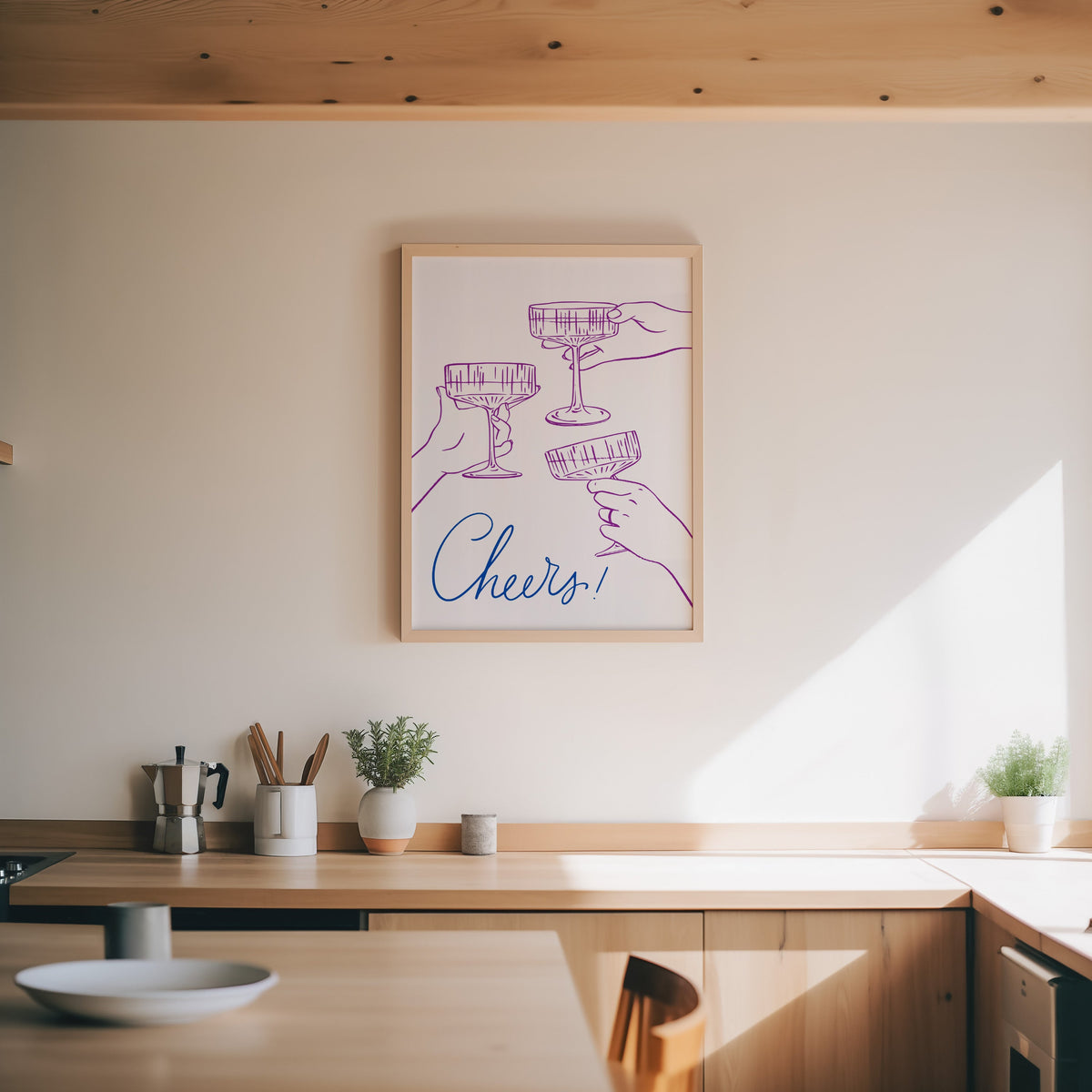 Cheers coupe glasses print in an oak frame above a wood counter with a moka pot and herbs