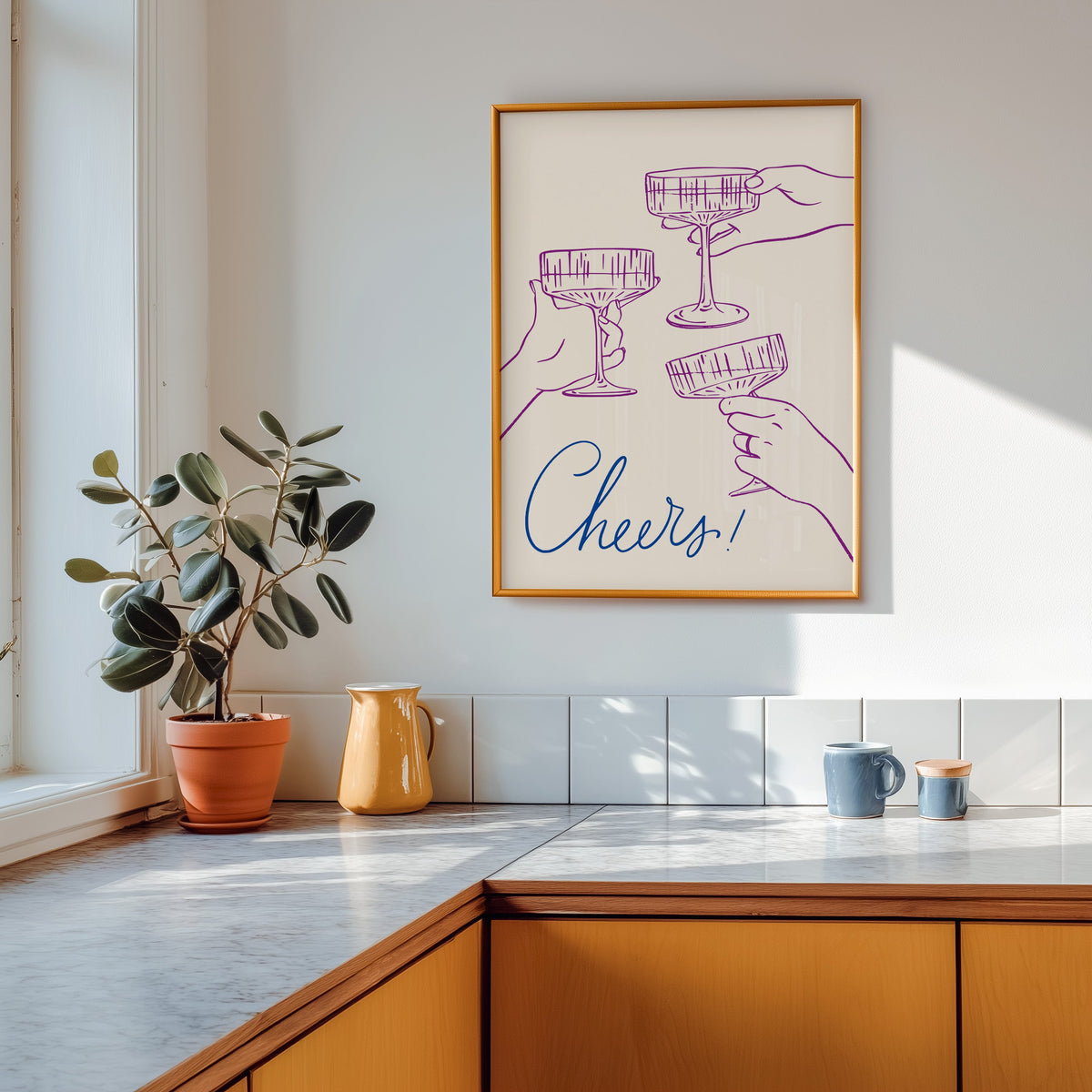 Cheers coupe glasses print shown in a gold frame above a marble counter with a yellow ceramic jug