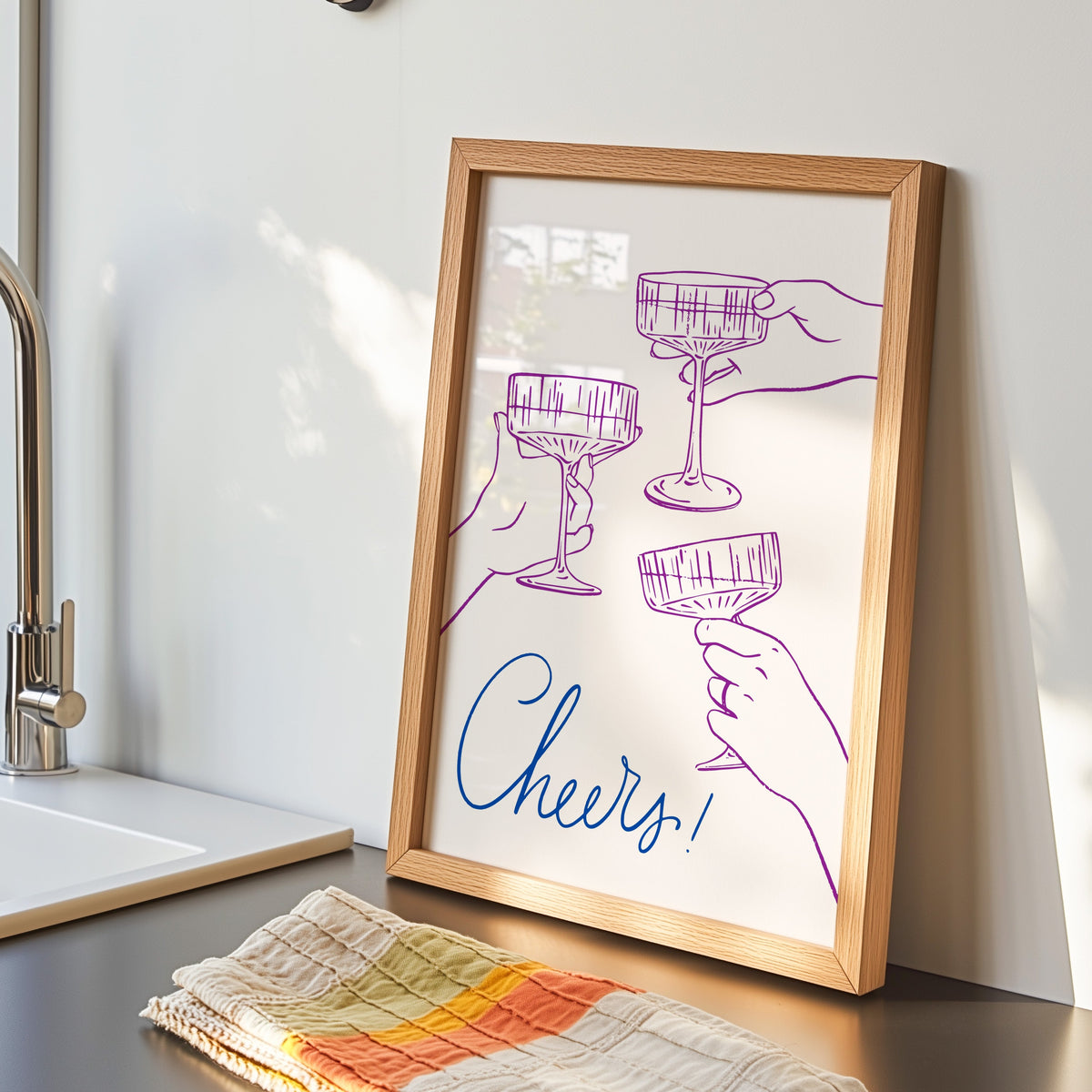 Cheers coupe glasses print in an oak frame by the kitchen sink beside a striped tea towel