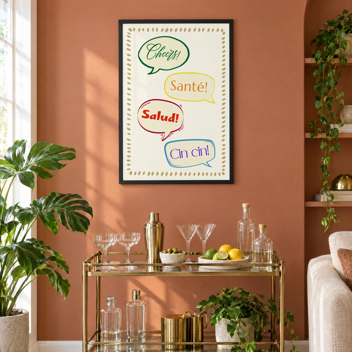 Cheers! Santé! Salud! Cin cin! speech bubbles print in a black frame on a terracotta wall above a brass bar cart with coupes and citrus