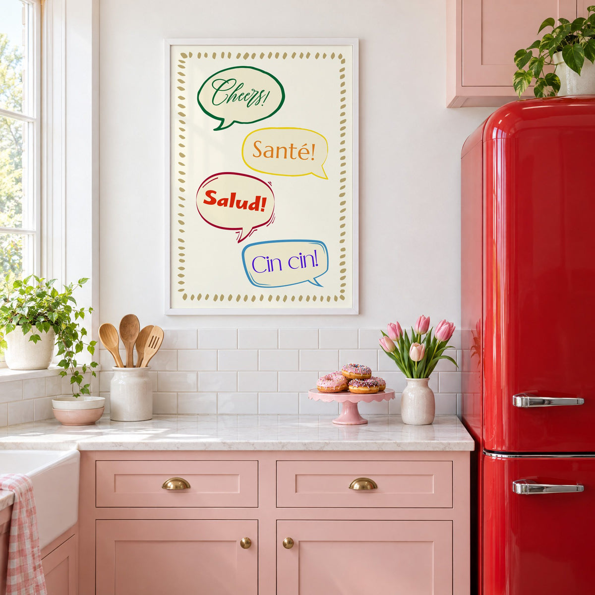 Cheers! Santé! Salud! Cin cin! speech bubbles print in a white frame above pink cabinets beside a red retro fridge