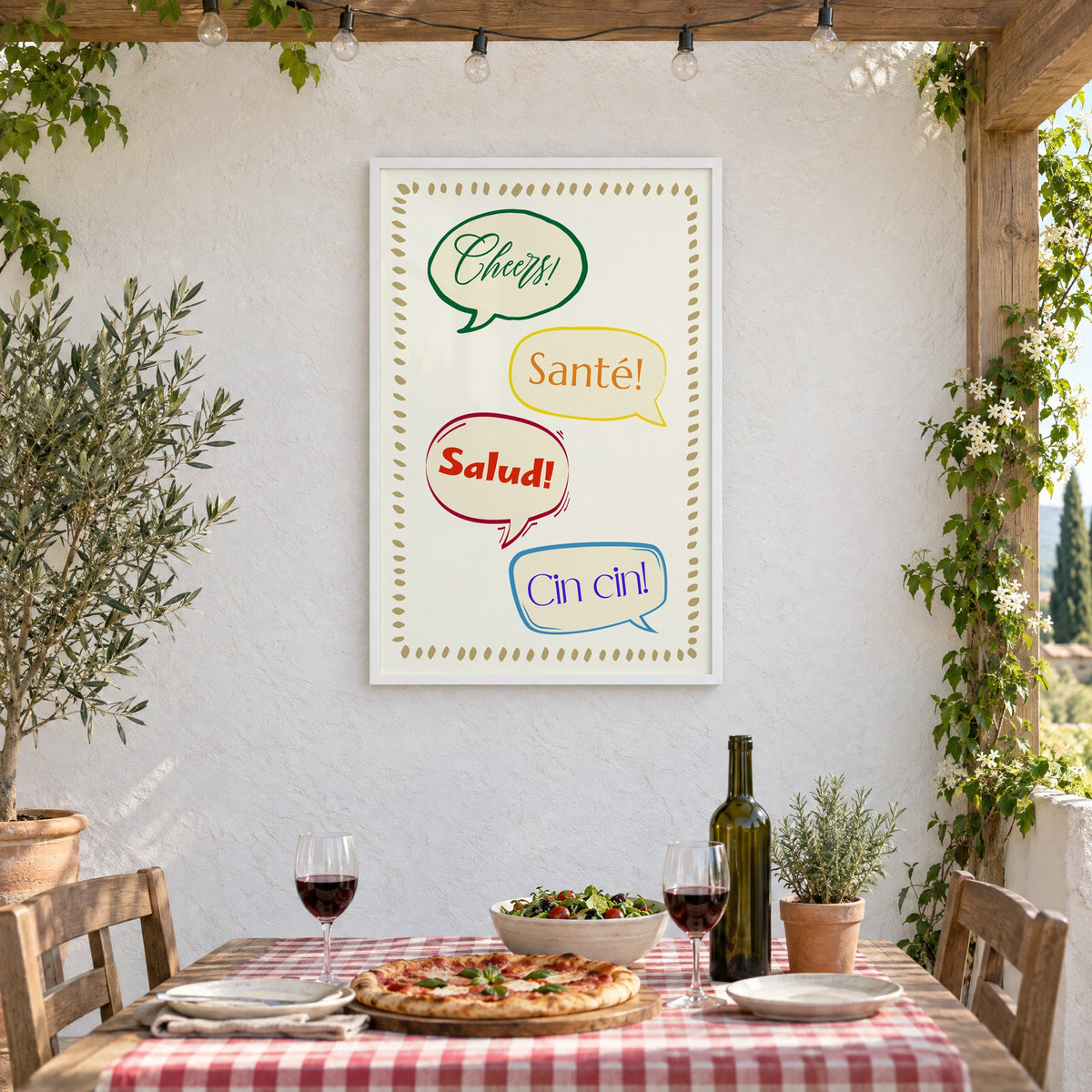 Cheers! Santé! Salud! Cin cin! speech bubbles print in a white frame on a stucco wall above a checked-cloth table with pizza and red wine