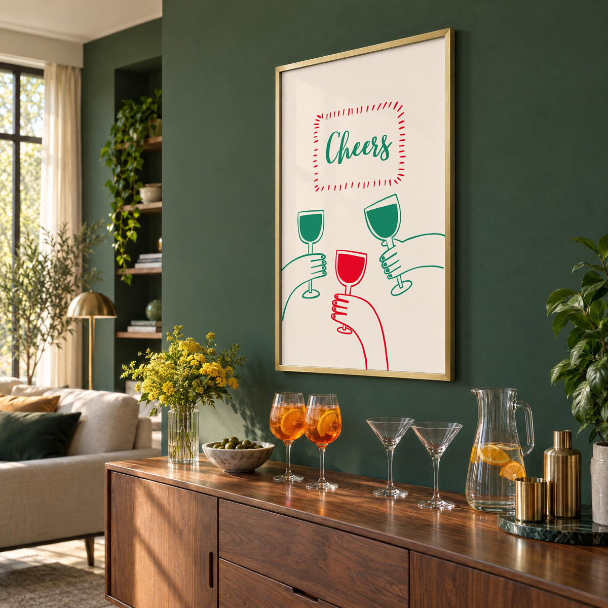 Cheers three hands wine toast line print in a brass frame on a bottle green wall above a sideboard with spritz and martini glasses, seen at an angle