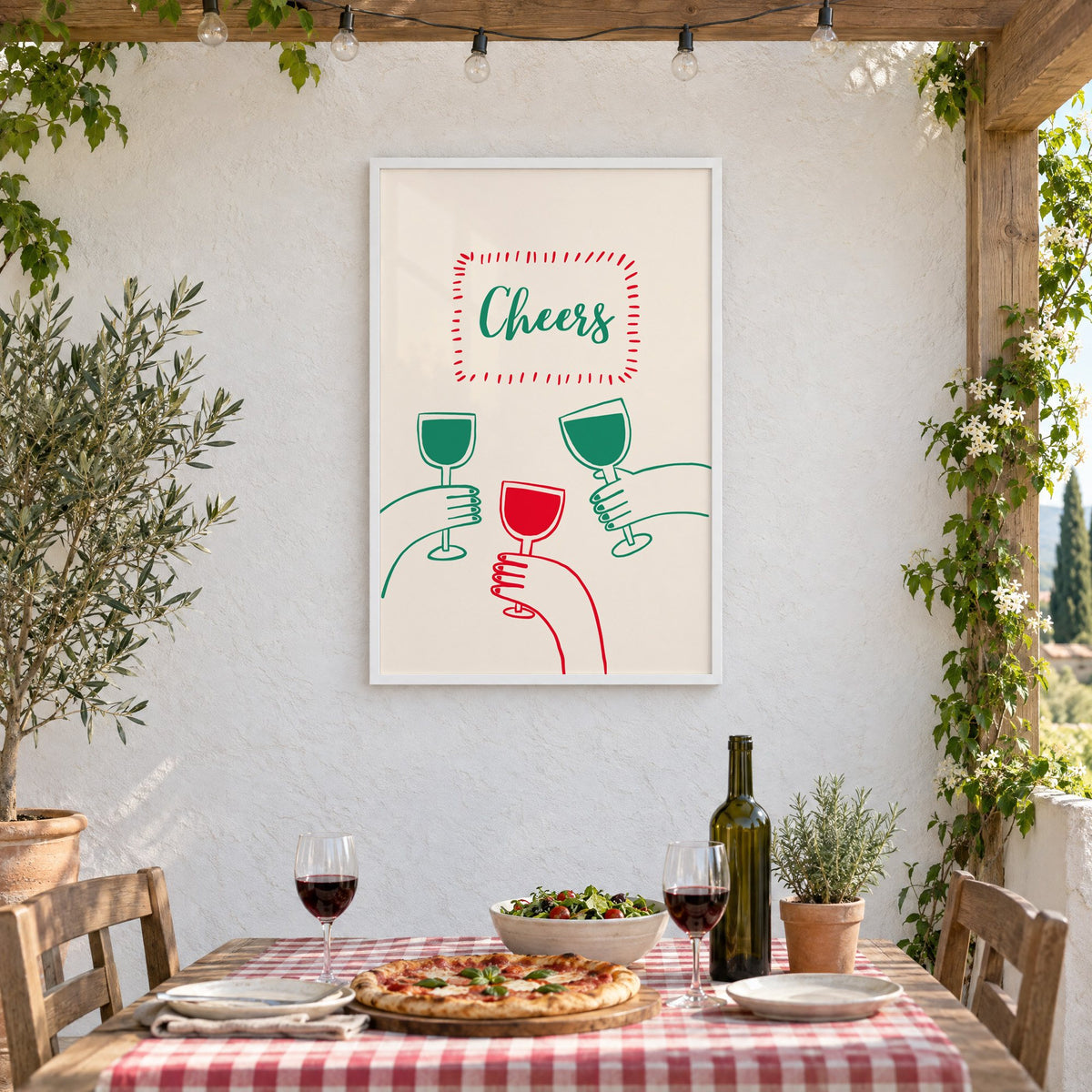 Cheers three hands wine toast line print in a white frame on a stucco wall above a checked-cloth table with pizza and red wine