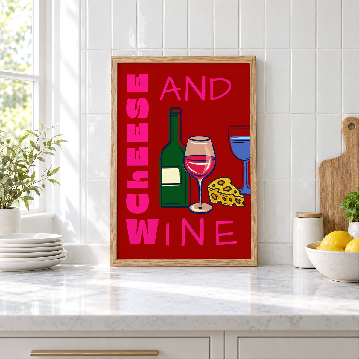 Cheese and wine bold red pink print in an oak frame leaning on a marble counter by white tiles and lemons