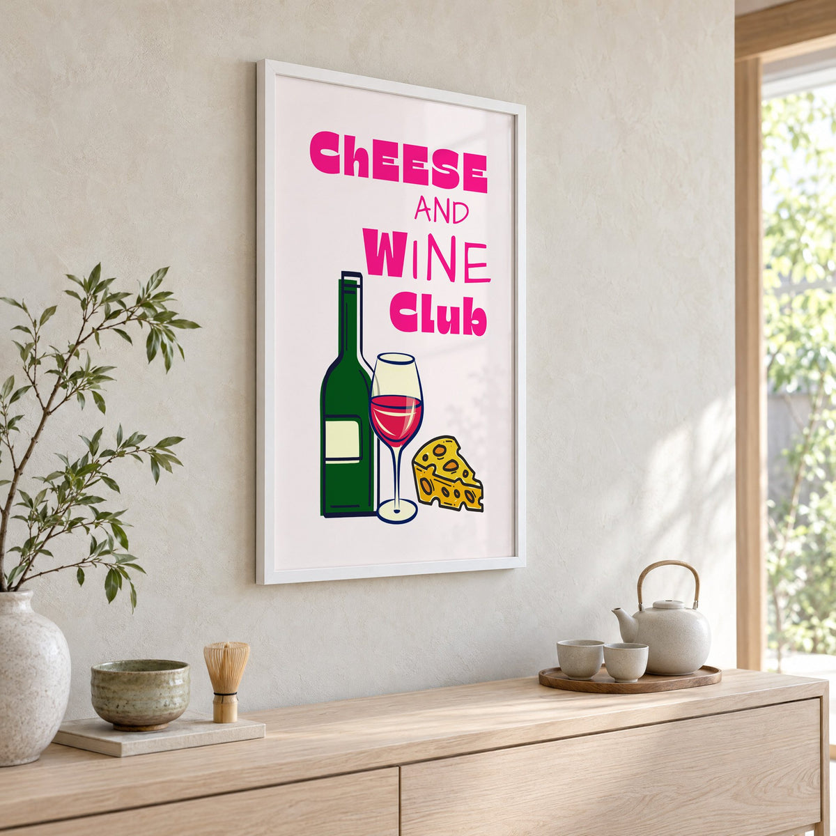 Cheese and Wine Club bottle print in a white frame above a pale wood console with a matcha tea set