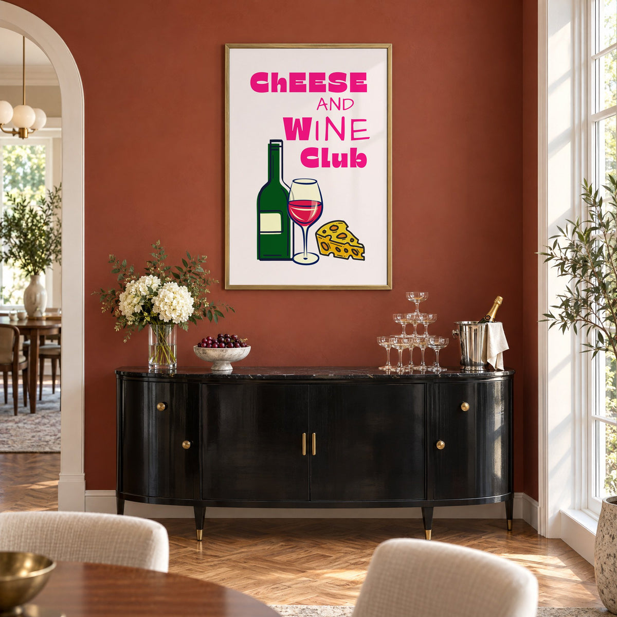 Cheese and Wine Club bottle print in a brass frame on a terracotta wall above a black buffet with a champagne tower